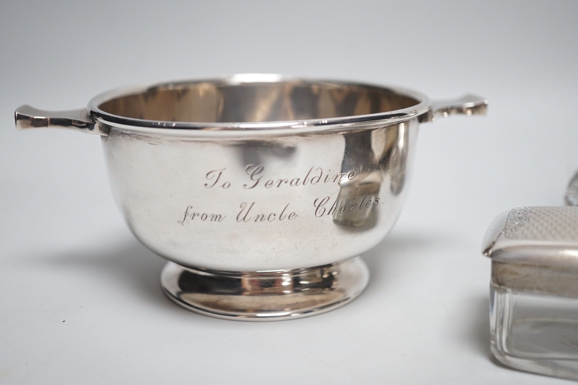 A George V silver two handled bowl, 14.6cm over handles, a white metal overlaid glass scent bottle (a.f.), a silver mounted blotter and a silver mounted glass toilet jar.
